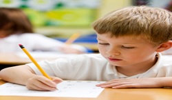 Primary school pupil sat at desk completing work or test
